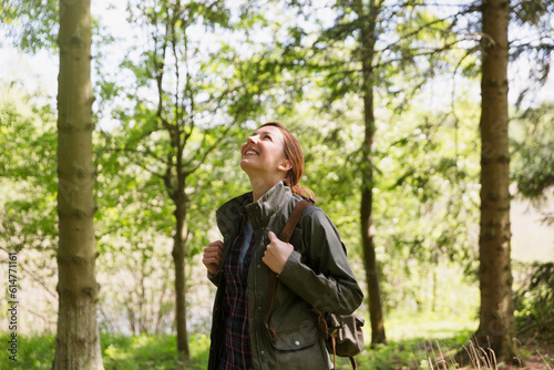 Smiling woman hiking looking up at trees in sunny woods