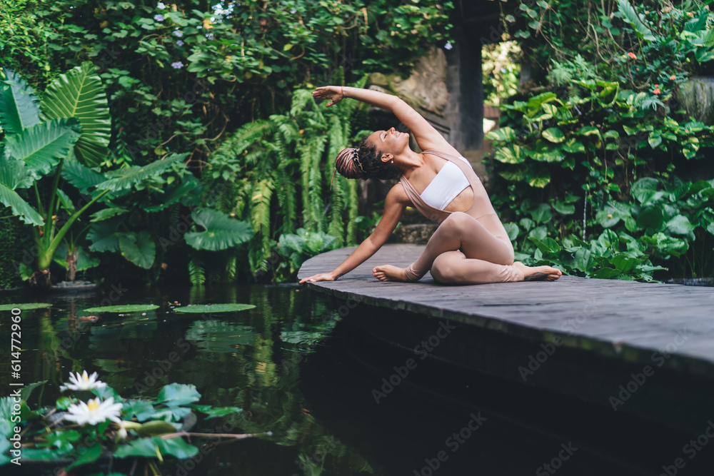 Fototapeta premium Harmony and meditation training during morning yoga at pond, happy Caucasian female yogi in sportswear sitting in flexible pose during hatha practice for exercising body concentration in asana