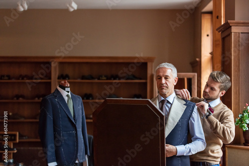 Tailor fitting businessman for suit in menswear shop photo