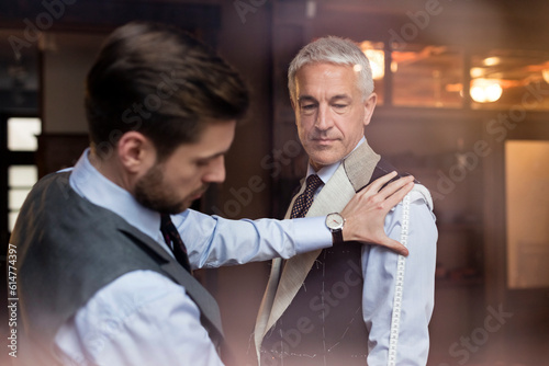 Tailor fitting businessman for suit in menswear shop
