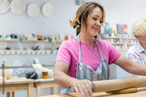 Smiling mature woman rolling clay with rolling pin in pottery studio