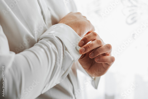 Portrait of a fashionable man fastening stylish cufflinks on the sleeves of his white shirt. Wedding day concept.