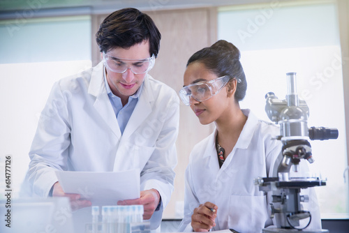 College students conducting scientific experiment at microscope in science laboratory classroom