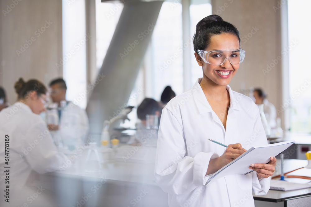 Portrait smiling female college student taking notes in science laboratory classroom Portrait smiling female college student taking notes in science laboratory classroom