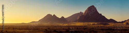 Mountain landscape of Spitzkoppe peaks in morning haze, wilderness of Namibia. Panorama of stone desert at on Damaraland sunrise, golden soft light of dawn mist. Travelling on wildlife of Africa.