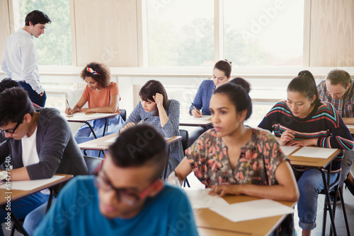 Professor watching college students taking test at desks in classroom