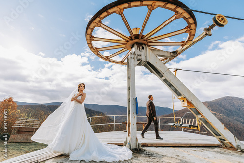 Married couple among mountains, bride looking back to groom, girl smiling, woman in white wedding dress, groom and brown suit
