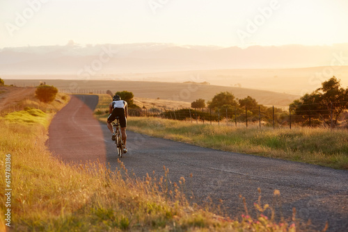 Male triathlete cyclist cycling on sunny rural road at sunrise photo