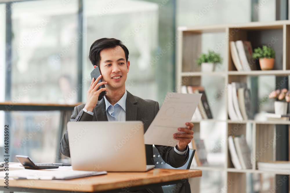 Smiling Asian Accountant person talking phone with client and makes financial report and studies annual figures, analyzes profits Smiling Asian Accountant person talking phone with client and makes financial report and studies annual figures, analyzes profits