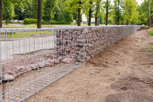 Construction of a gabion wall. The process of filling the basket with granite stones. Selective focus. photo
