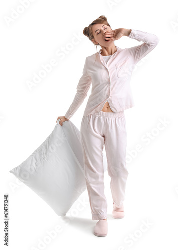 Beautiful woman in pajamas with pillow yawning on white background