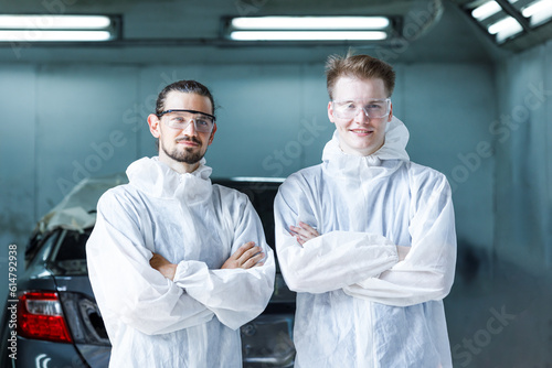 Fotografie Portrait of a team of two young men of professional car painter with protective clothing standing next to a car in front of a car painting room together