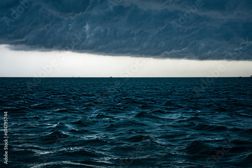 View of tropical ocean storm with menacing clouds and rain showering below, Light in the dark and dramatic storm clouds background © chokniti