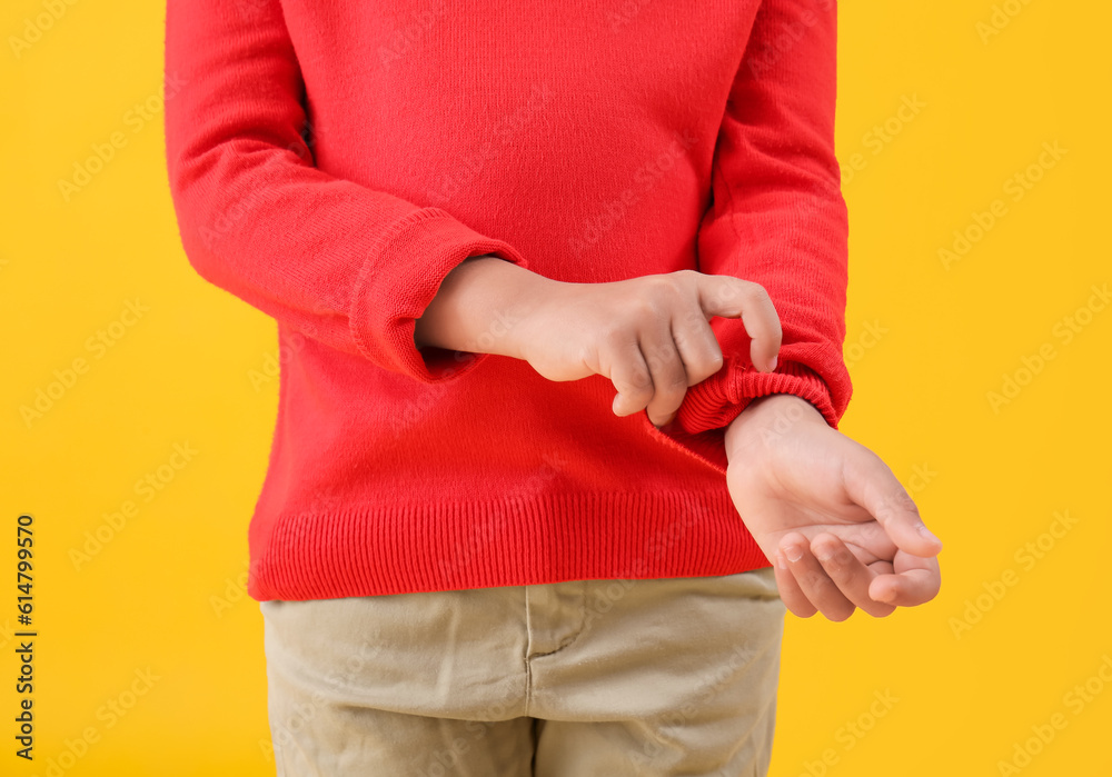 Little boy rolling up his sleeve on yellow background, closeup