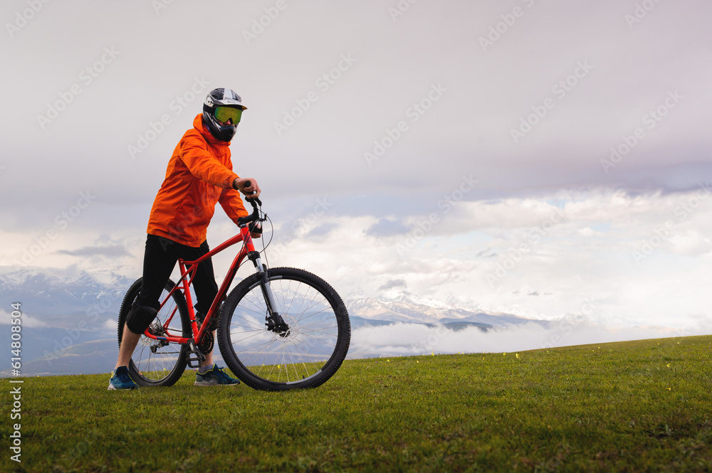 confident cyclist stands with his mountain bike on the edge of a cliff, wearing protective gear. Amazing views of the mountains and nature while doing sports confident cyclist stands with his mountain bike on the edge of a cliff, wearing protective gear. Amazing views of the mountains and nature while doing sports
