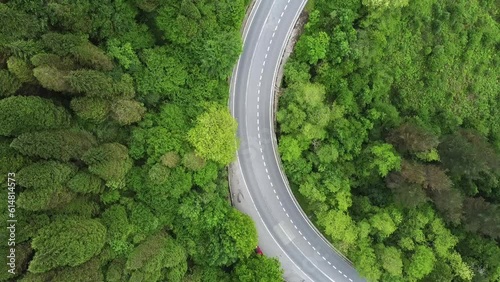 Aerial view of motorcycle driving on the rural road in the forest. A cinematic drone shot over a country road with a curve in the mountain.