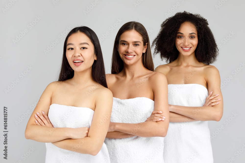Portrait of three young multiracial ladies posing wrapped in towels with folded arms, smiling at camera, grey background Portrait of three young multiracial ladies posing wrapped in towels with folded arms, smiling at camera, grey background