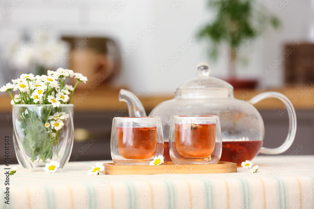 Wooden tray with teapot, cups of natural chamomile tea and flowers on table in kitchen Wooden tray with teapot, cups of natural chamomile tea and flowers on table in kitchen