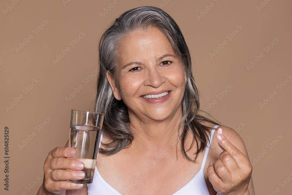 Happy european old woman with gray hair hold glass of water, vitamins capsule Happy european old woman with gray hair hold glass of water, vitamins capsule