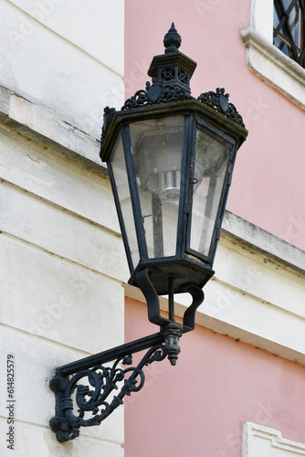 A black lantern with a lot of beautiful elements, located on the facade of a building painted in white and pink