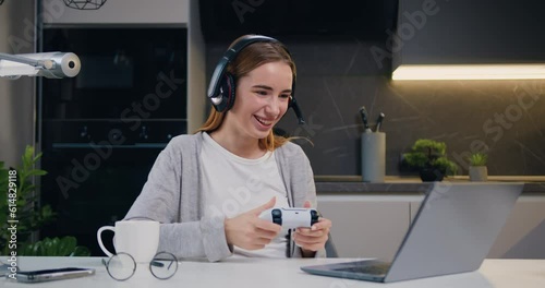 Good-looking excited joyful young caucasian girl in headset celebrating victory in video game on laptop with clenched fists and smile, spending shis leisure at living room photo