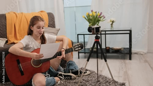 Young teenager girl with guitar making stream translation and teaching followers musical instrument playing tips. Pretty female guitaris making video for social media channel photo