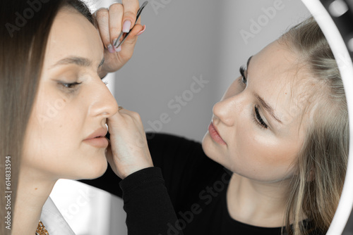 The photo conveys the skill of makeup artist who improves shape eyebrows  giving them sophistication and clarity. This process is an important step for creating impeccable image client in beauty salon