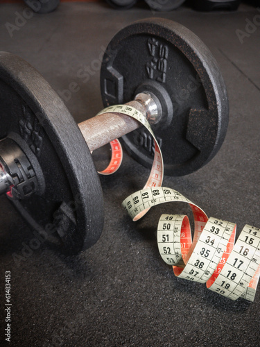 Close-up of 4.4lbs or 2Kg black rusty loadable dumbbell and measuring tape on the floor at the gym. Fitness, weight training or healthy lifestyle concept photo