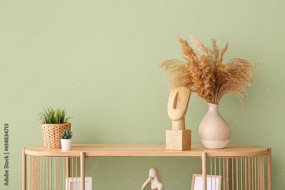 Modern shelving unit with pampas grass, houseplants and decor near green wall in room Modern shelving unit with pampas grass, houseplants and decor near green wall in room