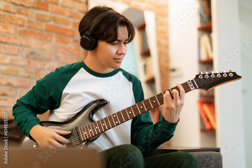 Korean Teen Enjoying Rhythm Playing Electric Guitar, Wearing Earphones Indoors