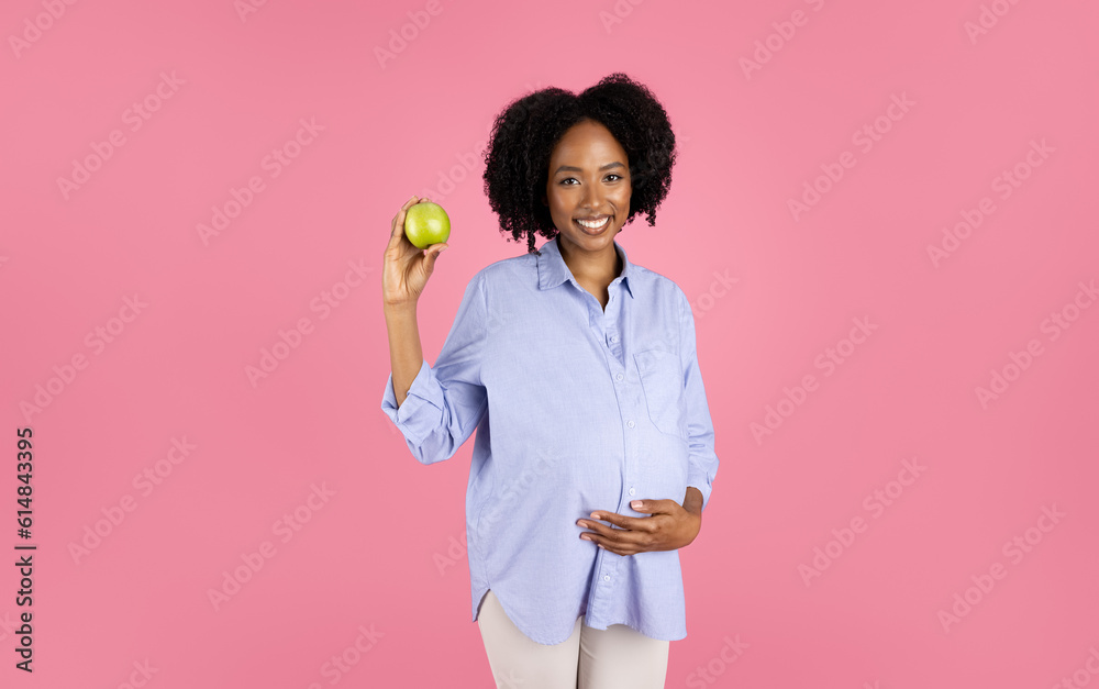 Smiling millennial african american curly pregnant lady in casual with big belly show green apple Smiling millennial african american curly pregnant lady in casual with big belly show green apple