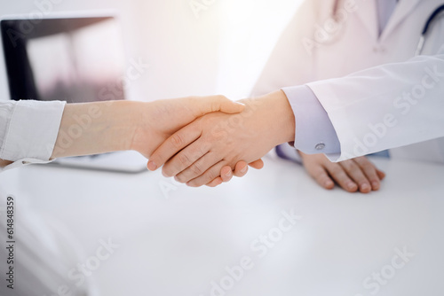 Doctor and patient shaking hands while sitting opposite of each other at the table in clinic, just hands close up. Medicine concept