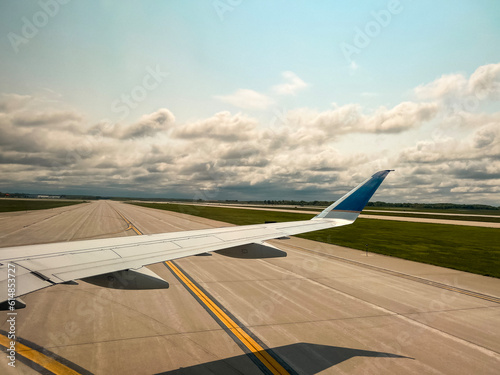 A commercial airplane is on the runway, waiting to take off. Views of the airplane wing and airfield. Passenger point of view, looking out an airplane window.