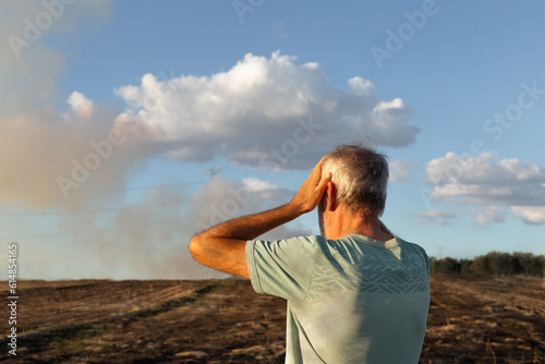Close-up of a man from behind looking at his burnt field.
