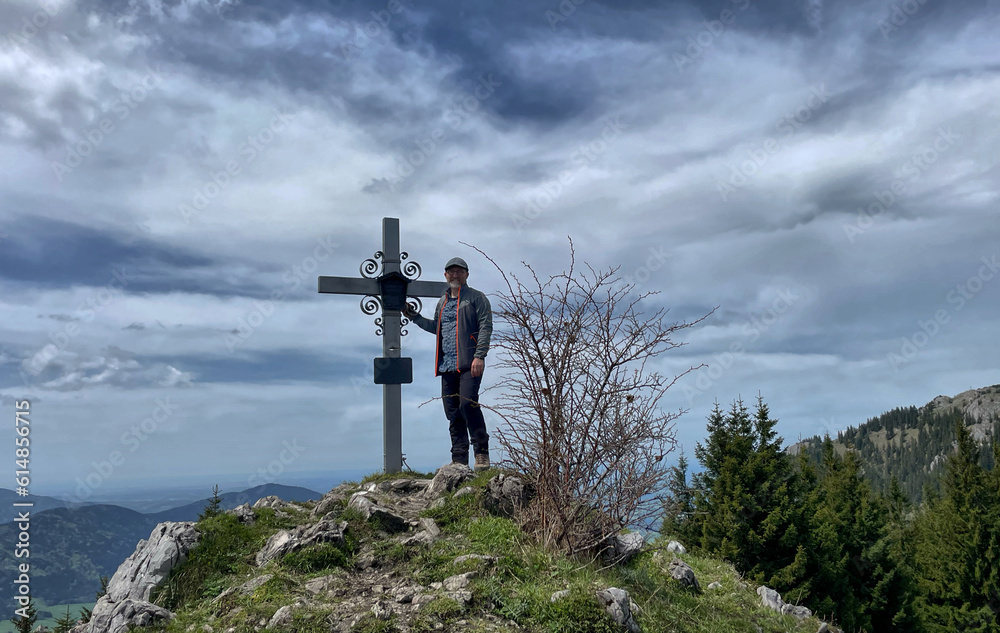 Obraz premium Bergwanderer (männlich) am Gipfelkreuz des Schweinsberg, Bayern, Deutschland, Alpen