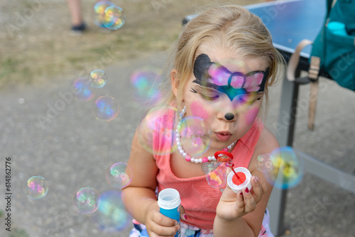 Little toddler girl having fun in a summer festival with face painting blowing bubbles