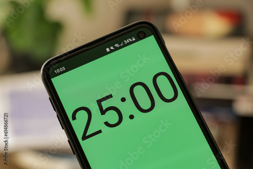 A phone with a green and white 25-minute timer to study with the pomodoro method on a blurry background. Perfect for students planning their time studying, doing homework, being productive.
