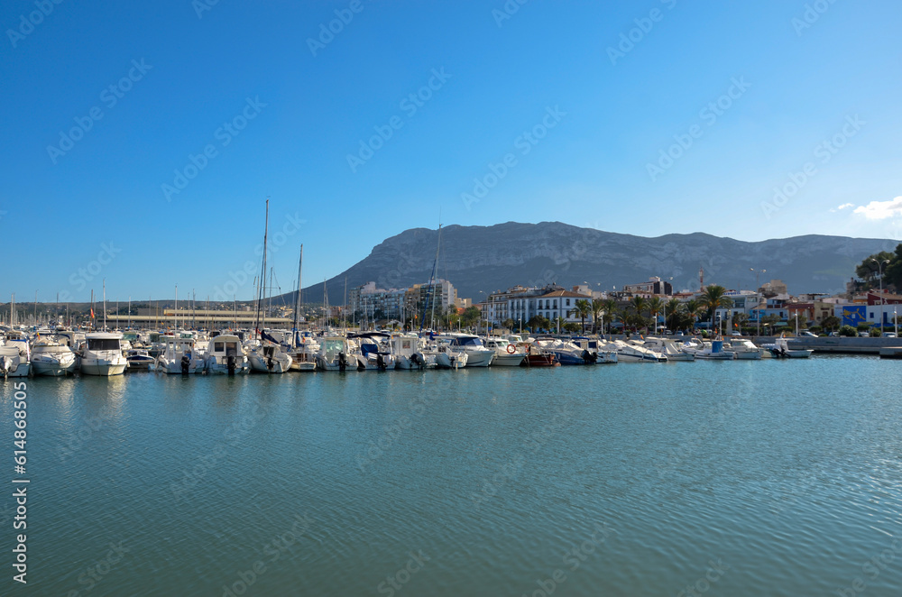 View of a pier of the yacht and sailing port of Denia with houses on the promenade and the mountainous coast in the background