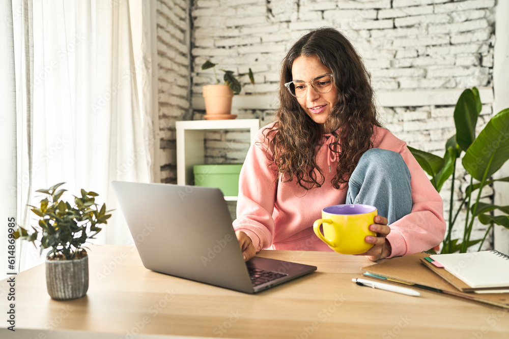 A young woman, focused and productive, working at her home desk with a laptop, sipping coffee, and feeling refreshed. A young woman, focused and productive, working at her home desk with a laptop, sipping coffee, and feeling refreshed.