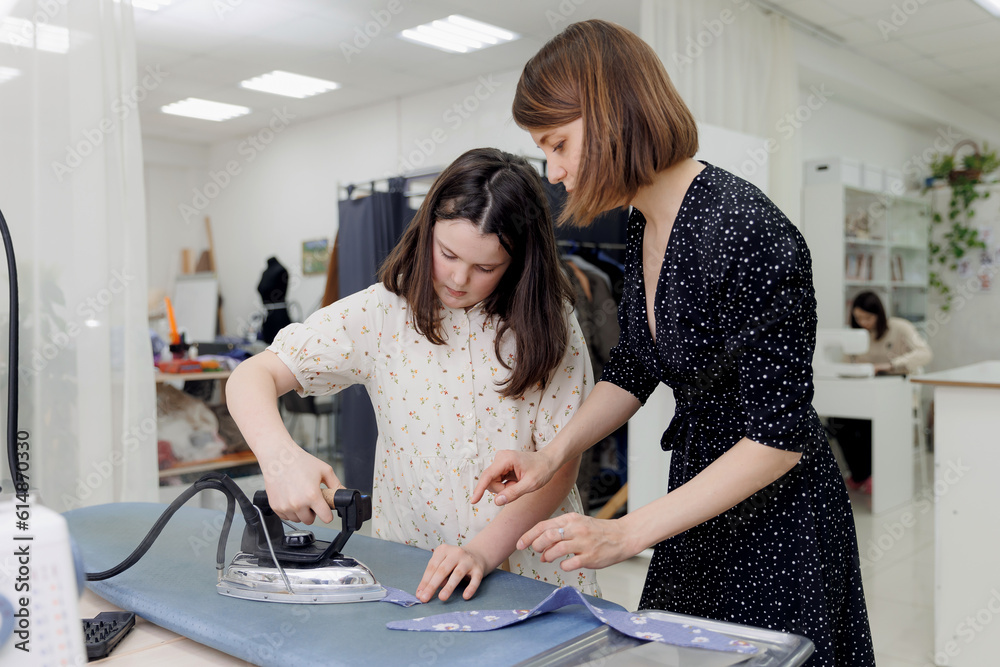 Dressmaker conducts sewing master class in school for two girl child. Smiling female designer or seamstress talking with children, education work Dressmaker conducts sewing master class in school for two girl child. Smiling female designer or seamstress talking with children, education work