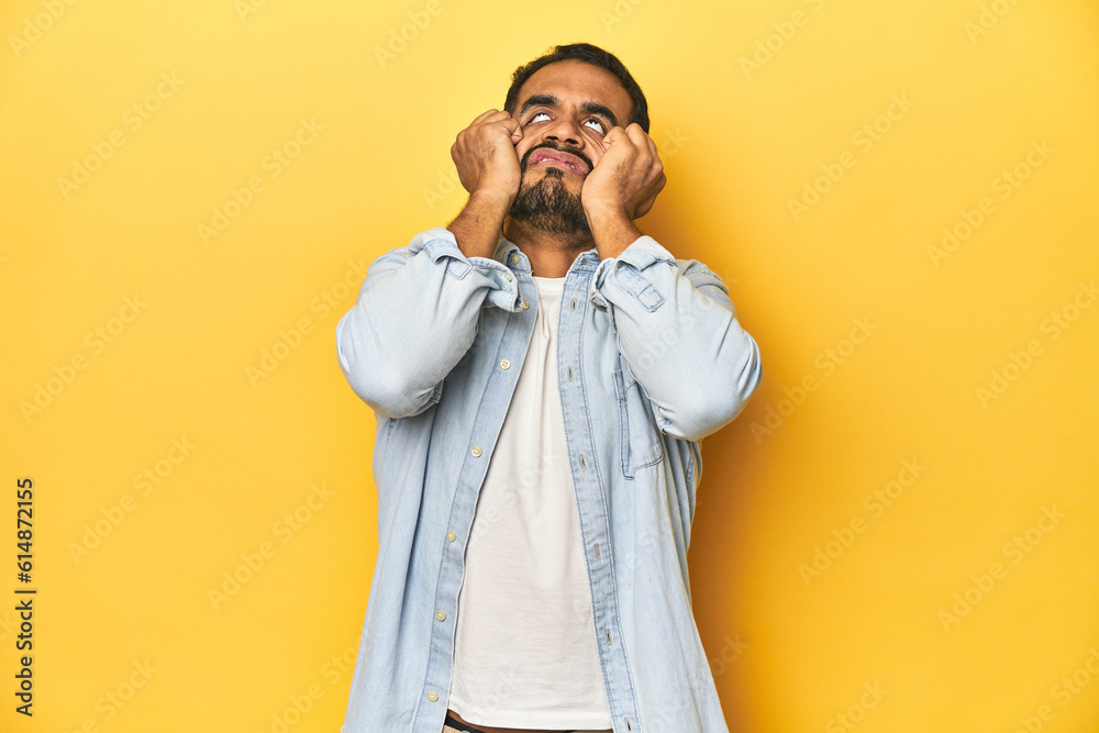 Casual young Latino man against a vibrant yellow studio background, crying, unhappy with something, agony and confusion concept. Casual young Latino man against a vibrant yellow studio background, crying, unhappy with something, agony and confusion concept.