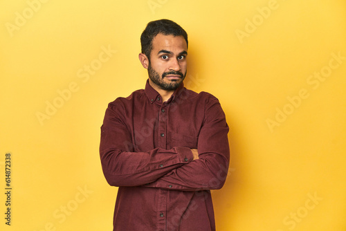 Casual young Latino man against a vibrant yellow studio background, suspicious, uncertain, examining you.