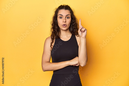 Sporty woman in active wear, yellow backdrop, having some great idea, concept of creativity.
