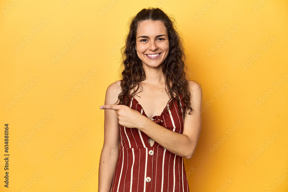 Young Caucasian woman, yellow studio background, smiling and pointing aside, showing something at blank space. Young Caucasian woman, yellow studio background, smiling and pointing aside, showing something at blank space.