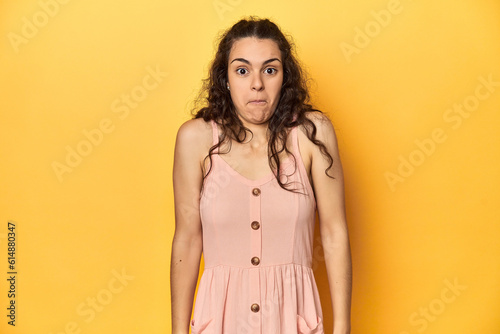 Young Caucasian woman, yellow studio background, shrugs shoulders and open eyes confused.
