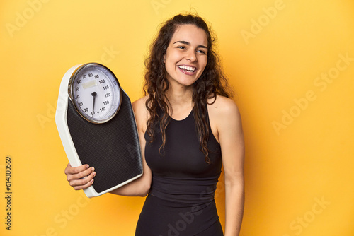 Young Caucasian woman with scale, weight management concept, yellow background.