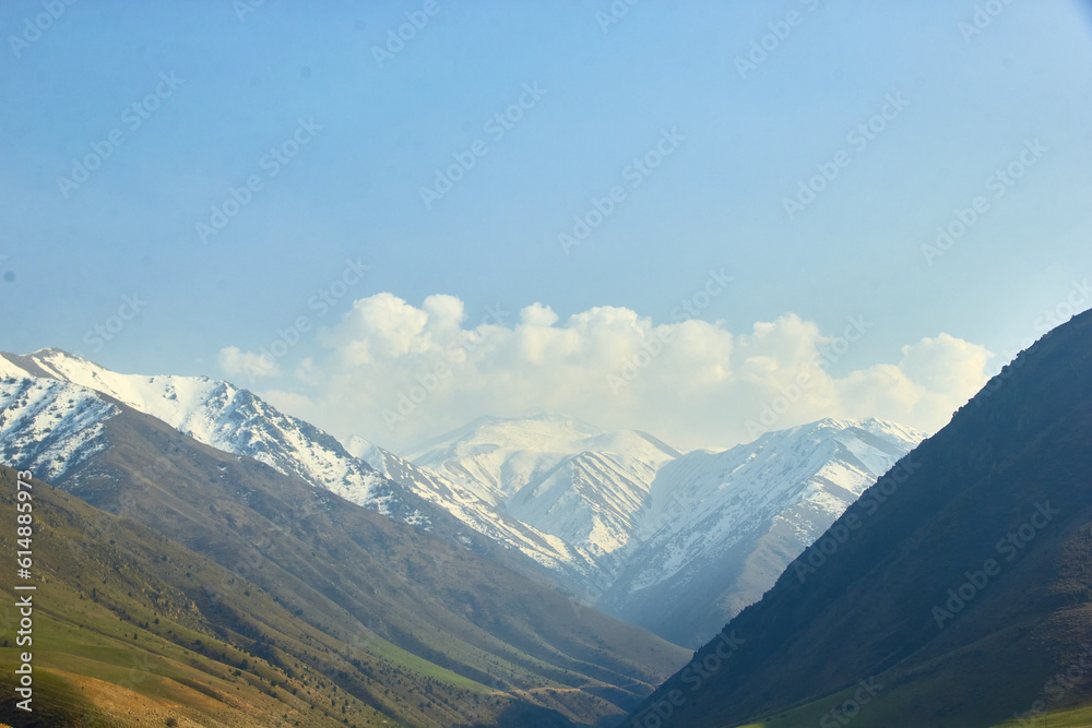 landscape against a mountain backdrop of high mountain ranges with snow-capped mountains and a blue sky with clouds