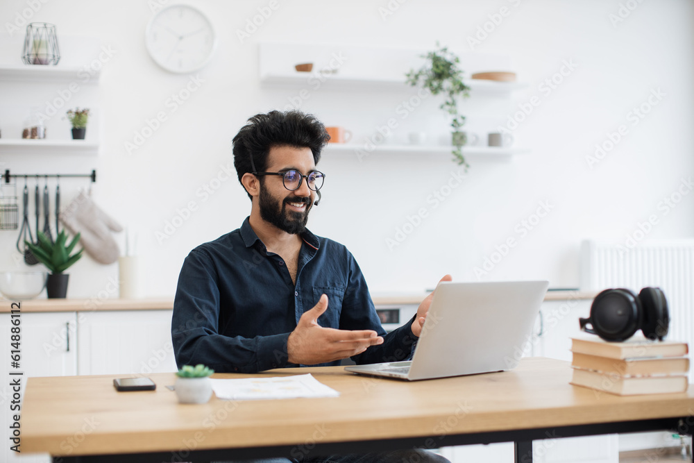 custom made wallpaper toronto digitalYoung indian man in wireless headset conducting online meeting with teammates via laptop in kitchen interior. Serious freelance worker showing effective communication ability during web conference.
