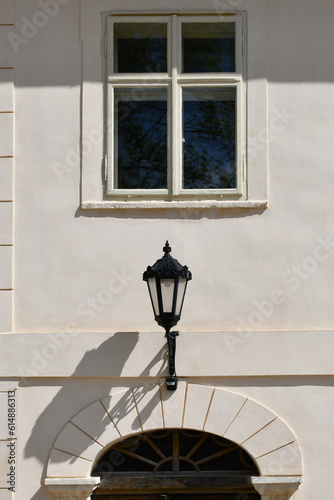 A lantern with a lot of beautiful elements,located on the facade of building,painted in a light color from a pastel palette,between the second floor window and the semi-oval frame of the entrance area