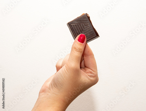 Foto Close-up of a woman's hand with red fingernails holding an ounce of dark chocolate with almonds on a white background